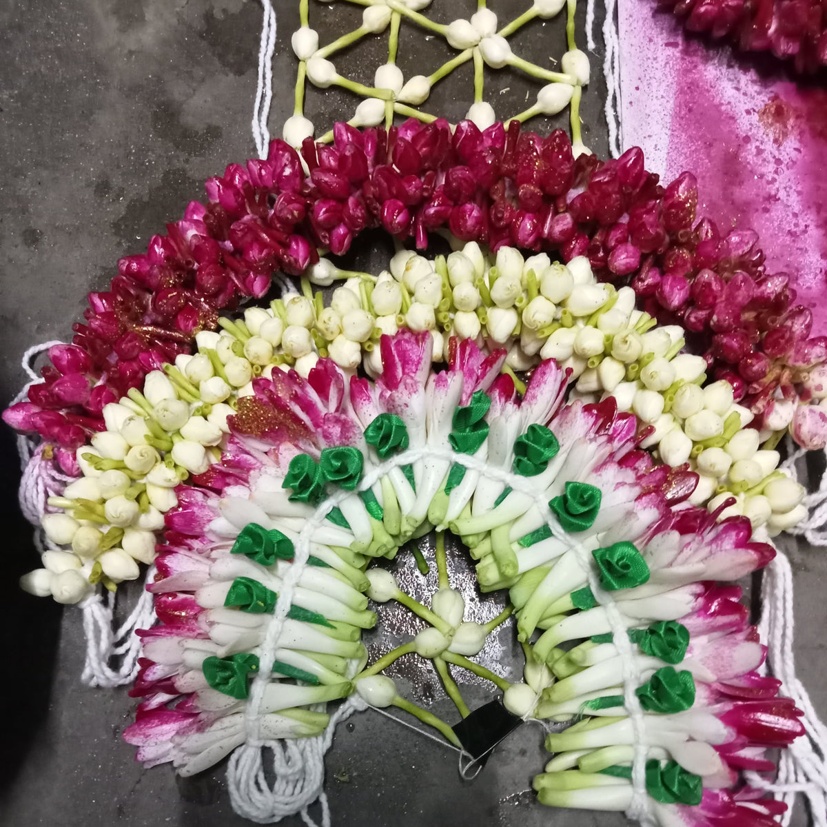 A bridal flower jada head piece laid flat: a crescent of magenta and white buds, jasmine and tuberose with white tassels