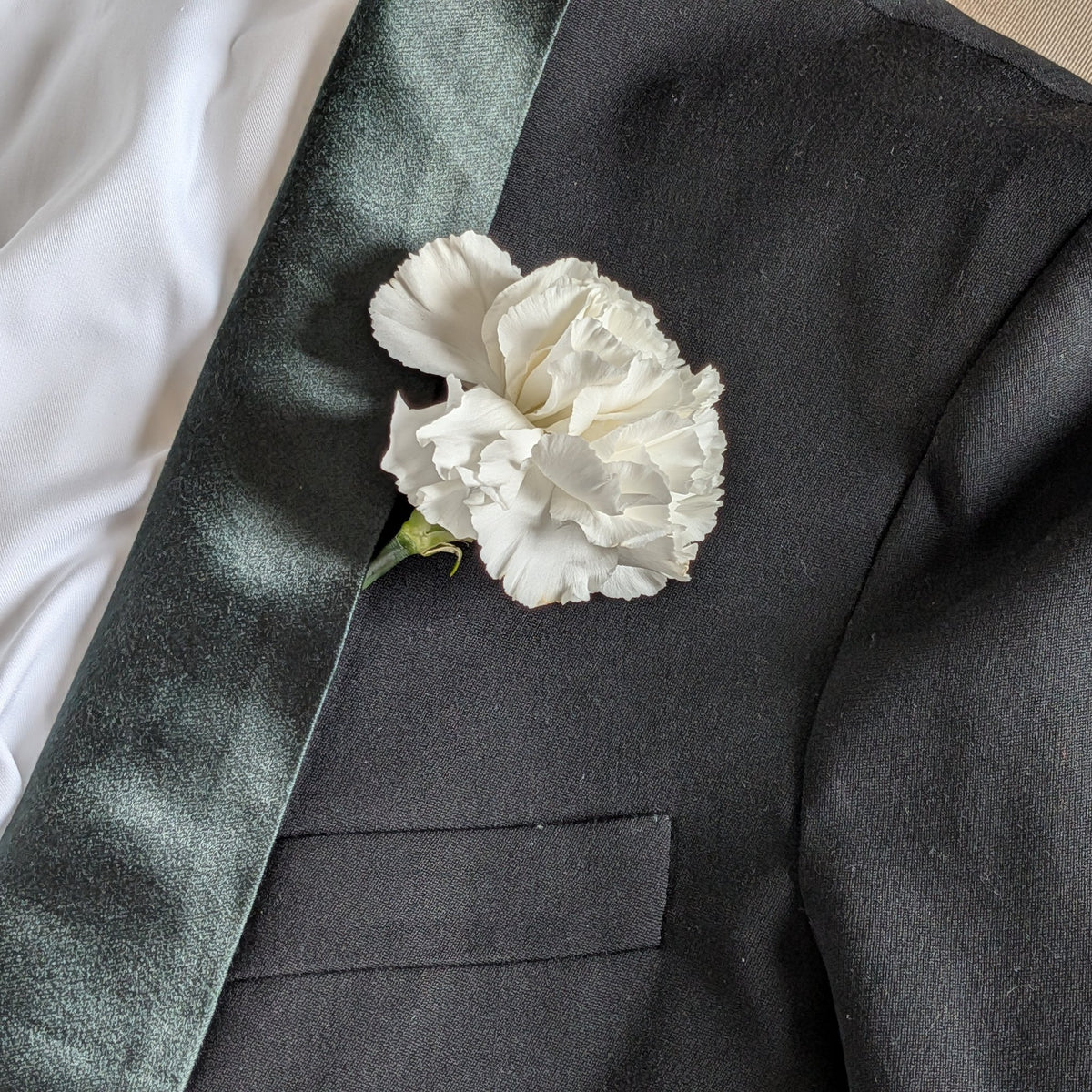 A white carnation boutonniere on the lapel of a dark jacket