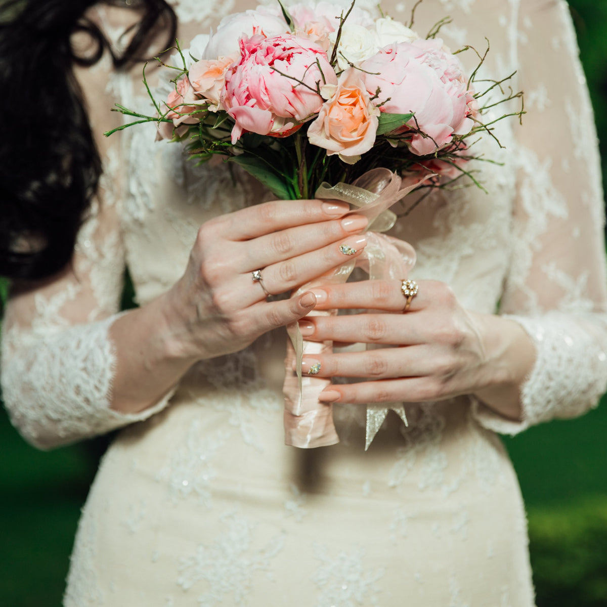 A bride holding a hand-tied bouquet of pink peonies and roses