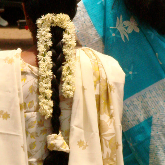 Strings of white jasmine looped down a long braid, seen from behind