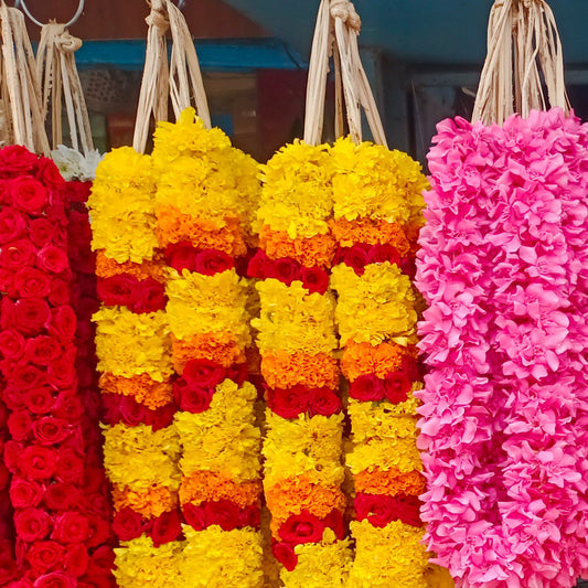 Yellow chrysanthemum garlands banded with orange and red, between a red rose garland and a pink garland, at a market stall