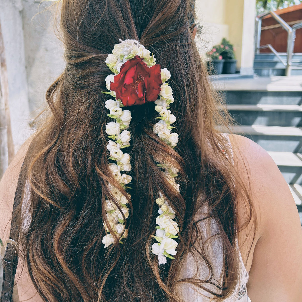 Back view of long hair decorated with a red rose and two hanging strands of jasmine buds