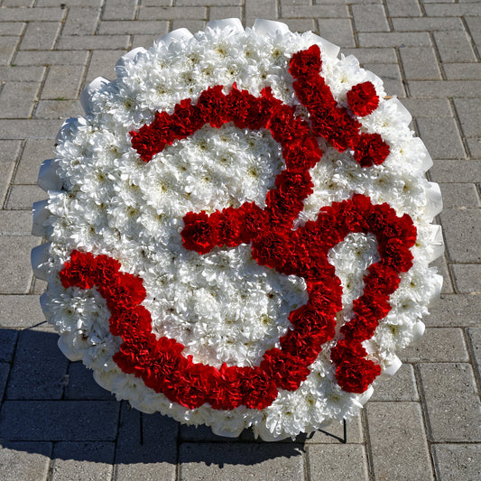 A round fresh-flower tribute of white chrysanthemums with the Om symbol in red carnations, on a stand