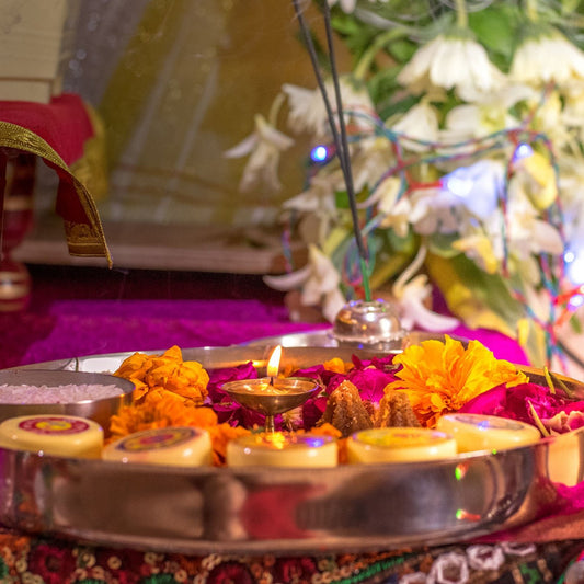 A pooja plate with marigolds, roses, small lamps and a lit diya
