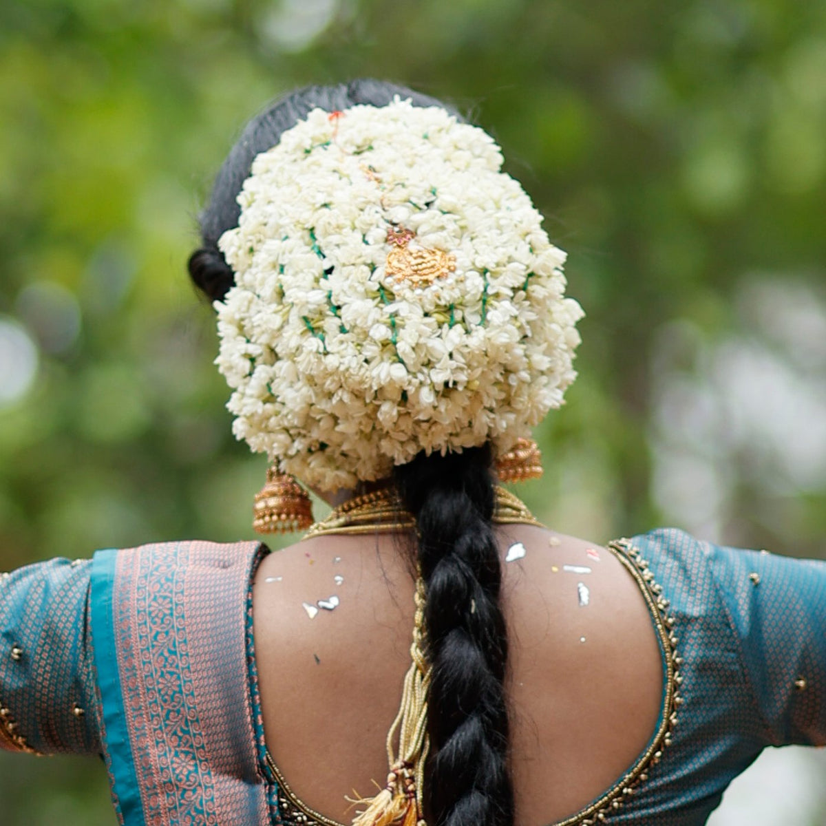 A bun covered in white jasmine buds above a long braid, seen from behind