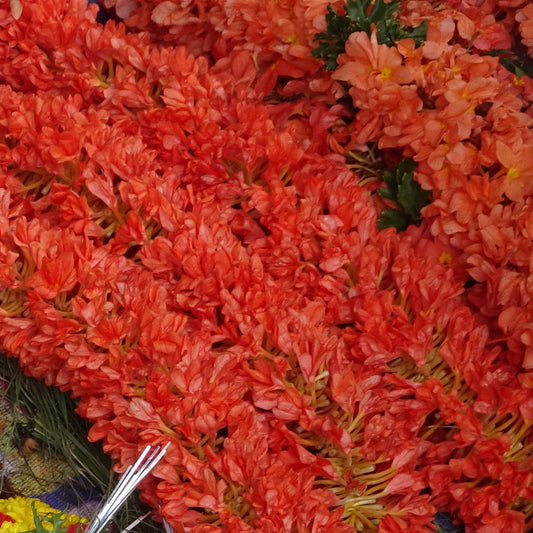 Strings of orange kanakambaram (crossandra) flowers piled at a market stall