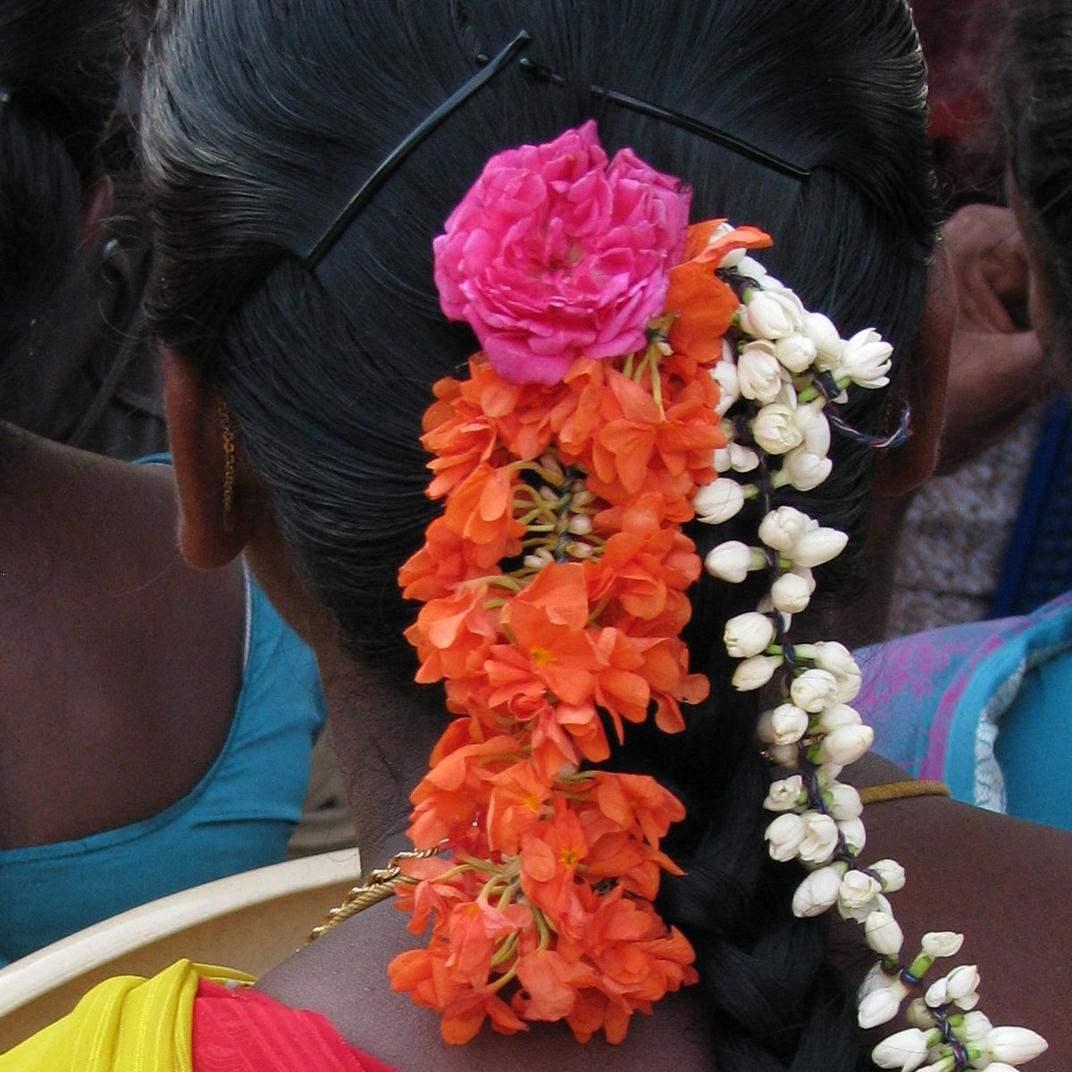 Orange kanakambaram and white jasmine strands with a pink rose pinned in a woman's hair, seen from behind