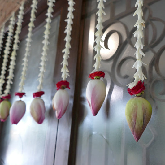 A row of white tuberose strands, each ending in a red rose and a lotus bud, hanging across a door