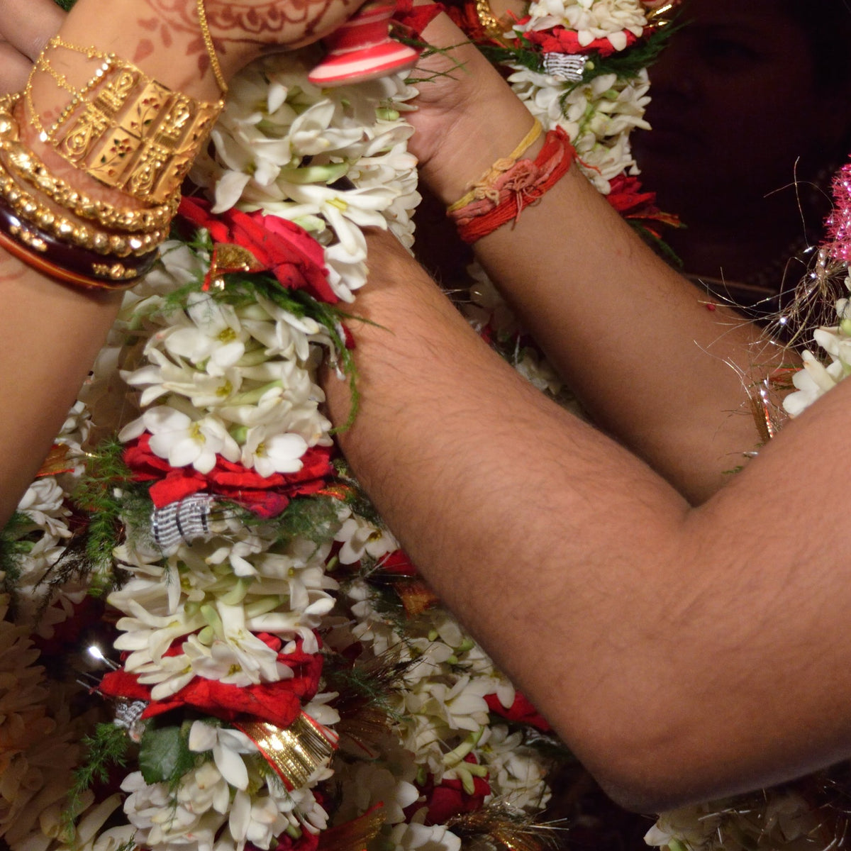 Garlands of white flowers and red roses being exchanged at a wedding, seen at the hands
