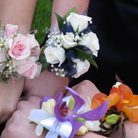 Fresh-flower wrist pieces of pink roses, white roses and purple and orange orchids worn on several wrists