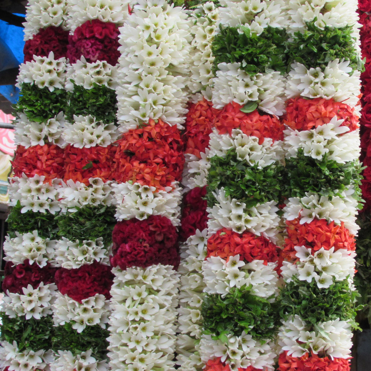Matching white garlands banded with red, orange and green, hanging side by side at a flower stall