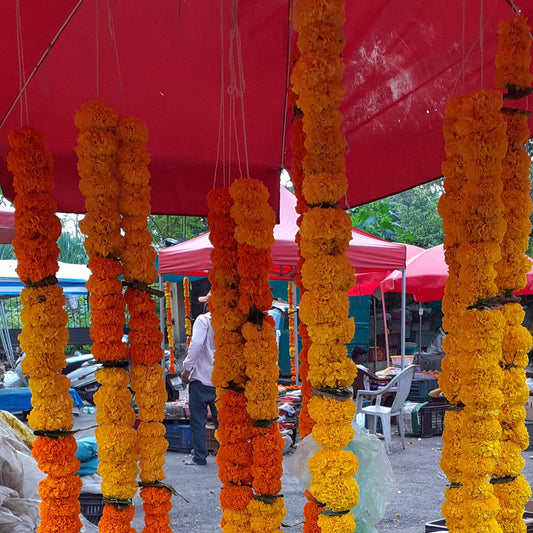 Long orange and yellow marigold garlands hanging under a red market umbrella
