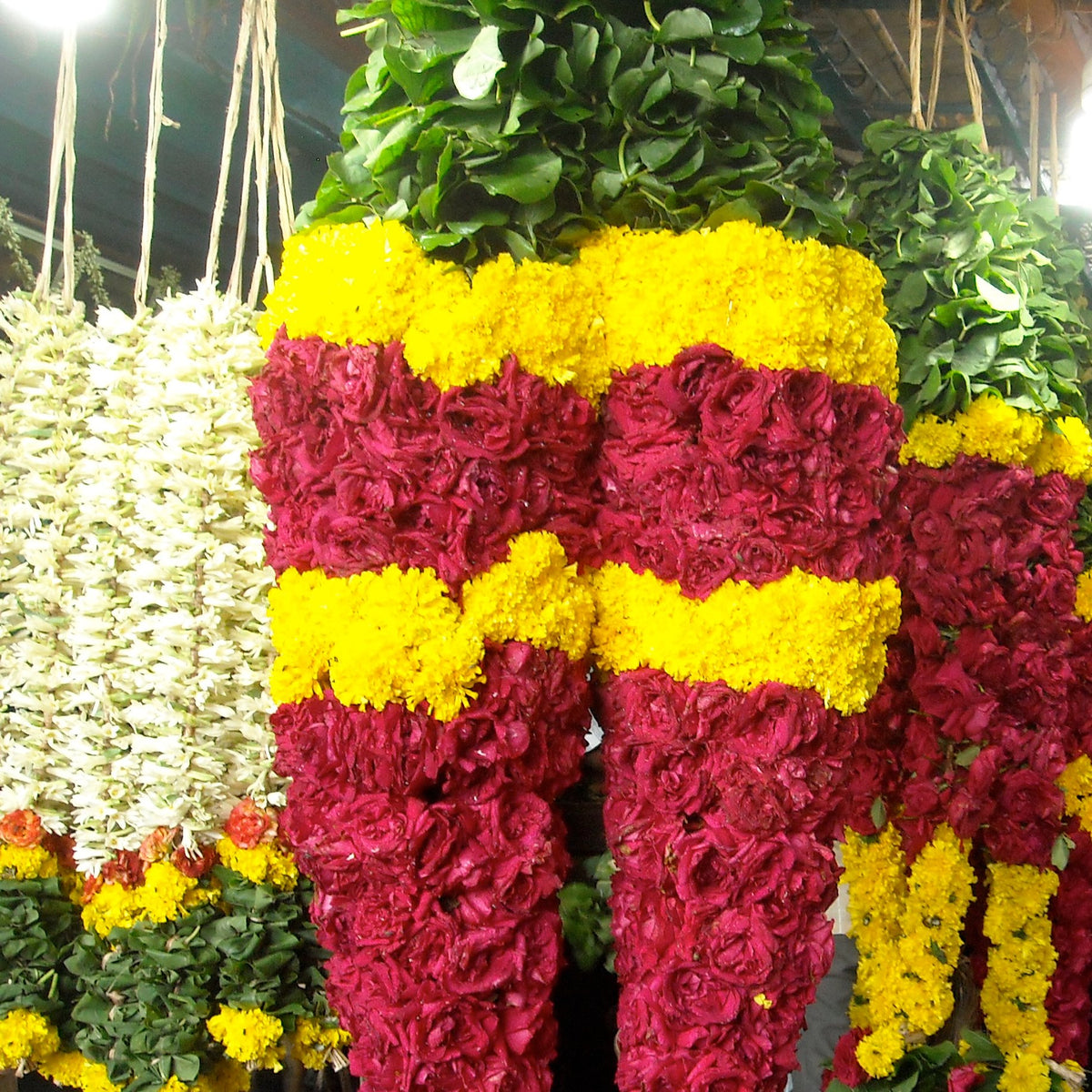 A matching pair of thick red rose garlands with yellow marigold bands, hanging at a flower market