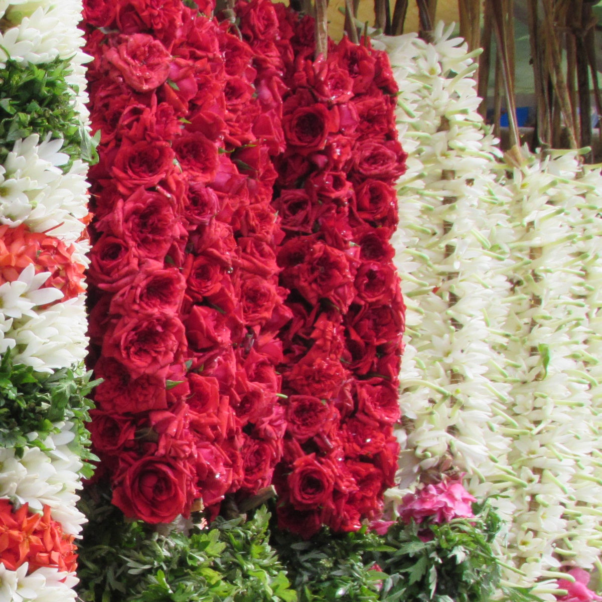 A thick red rose garland hanging between white tuberose garlands at a flower stall