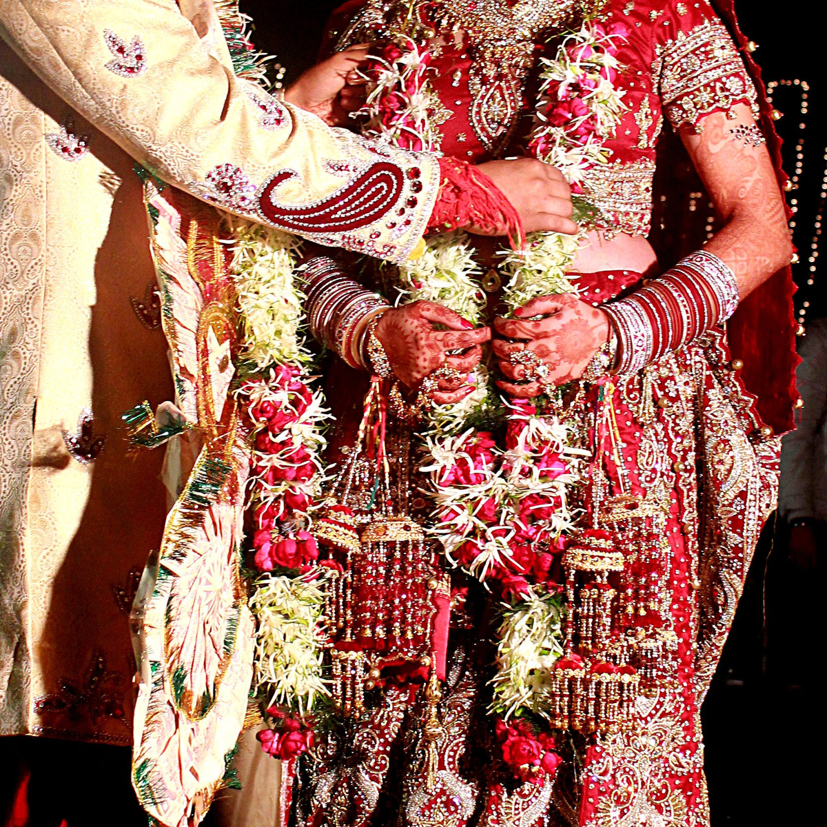 A bride and groom's hands and slim garlands of white tuberose and pink roses at a garland exchange