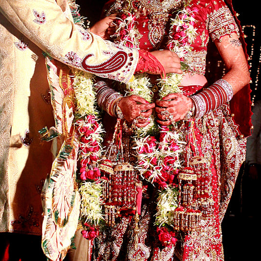 A bride and groom's hands and slim garlands of white tuberose and pink roses at a garland exchange