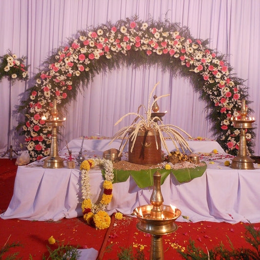 A wedding stage with an arch of pink and white gerberas, brass oil lamps and a coconut flower in a para